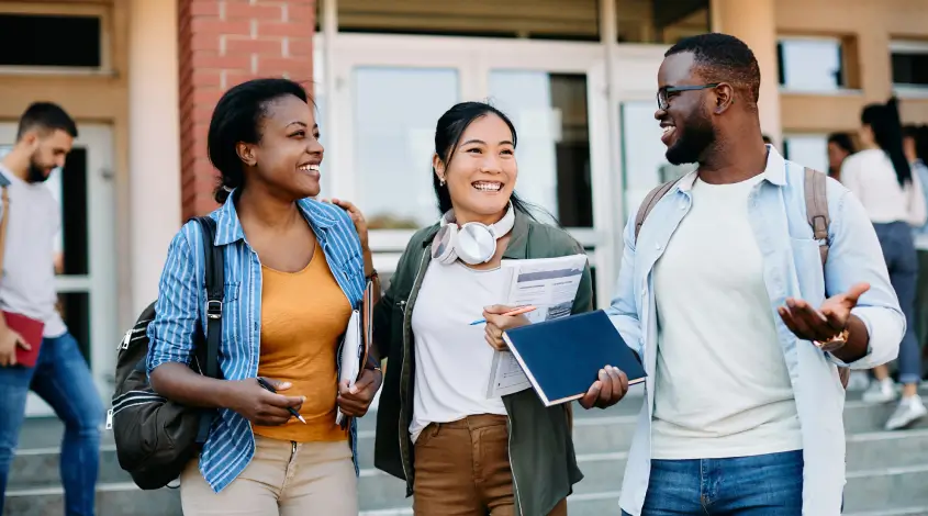three friends smiling outside of a school building